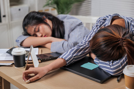 Young women business colleagues work long hours, online home office team feeling exhausted, sleeping on desk from overwhelming learn tasks, requiring rest and calm moments.の写真素材