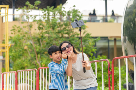 Mother, child, woman, son, family people enjoy summer day, parent takes selfie on city street, making heart hands gesture with big smiles, capturing memories together outdoors.の写真素材