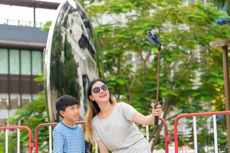 Mother and young son enjoy summer city street, woman parent child people family capture cheerful urban outdoor activity with phone selfie stick.の写真素材