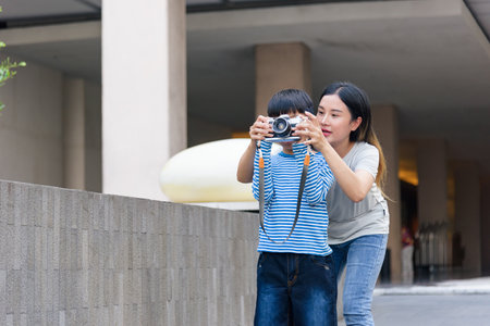 Mother, child, summer city family woman, parent guides young son exploring urban street, teaching photography skills with camera, sharing joyful outdoor activity and learning together.の写真素材
