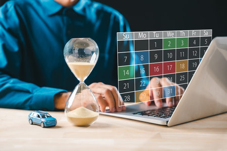 Person calculates car loan finance payment schedule on laptop, hourglass shows passing time for...
