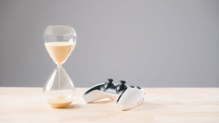 Video game controller sits beside flowing sand hourglass, hour glass shows limited play opportunity, reminding gamer concept for responsible time management.の写真素材