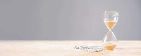 Hourglass time, money, global business finance economy concept shows sand flowing near dollar bills,...