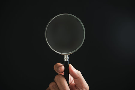 Hand holding a magnifying glass against a black background. The glass is slightly dusty.の写真素材
