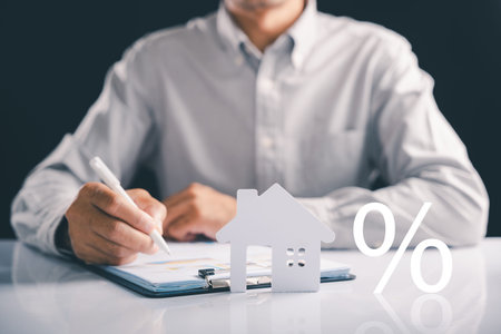 Considering a mortgage for your next home, this image shows a man analyzing paperwork with a house figure, investment and the percent symbol, illustrating real estate business and another mortgage.の写真素材