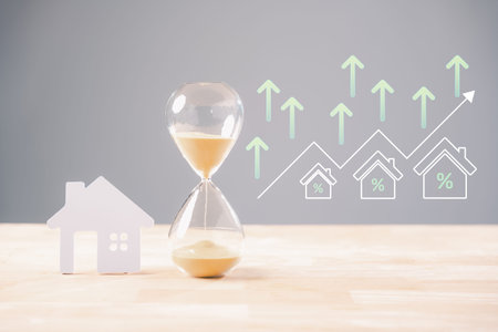 Hourglass time house mortgage real estate concept shows sand flowing near home building cutout,...