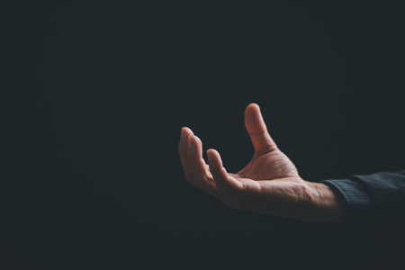 A hand with an open palm, reaching out on a dark background.  The hand is illuminated, highlighting...