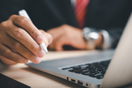 Close-up of a hand holding a white pen over a laptop keyboard. The focus is on the pen.