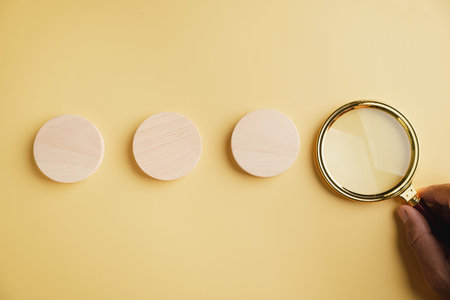 Three wooden circles on a yellow background, next to a magnifying glass.
