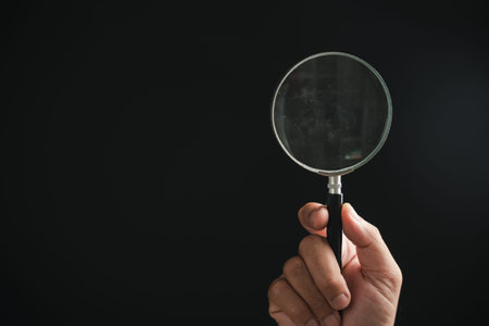 Hand holding a magnifying glass against a black background.