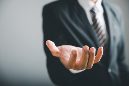 Closeup of a businessman's open hand, fingers extended, against a blurred background of his suit and...