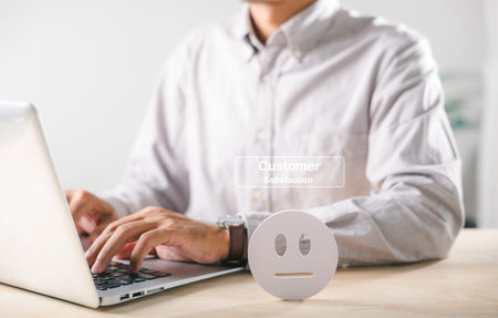 Neutral customer satisfaction feedback icon represents survey, man typing on laptop actively completing online business service quality review.の写真素材