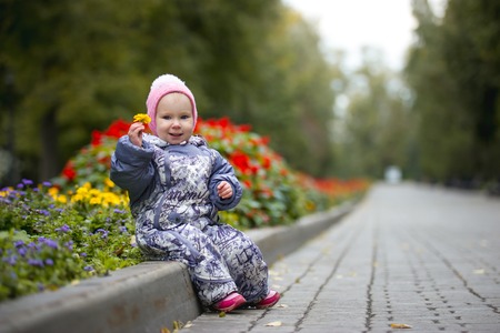 Portrait of child - little girl with fallen leaf walking in autumn park: baby sitting in the alley, telephoto shotの写真素材