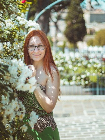Young beautiful pretty woman with red hair and glasses posing in Flowers garden, Roma, Italy, telephotoの写真素材
