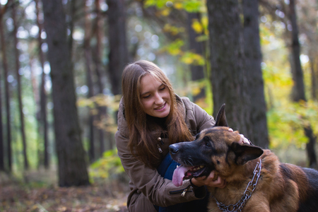 Young cute smiling girl playing with German Shepherd dog outdoors in the autumn forest, telephotoの写真素材