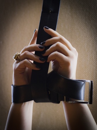 Girl has hands bound with leather belt - illustrate pretty nail manicure, extremely close upの写真素材
