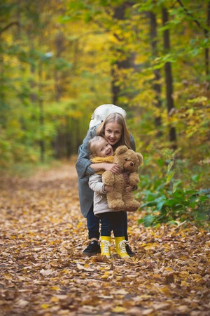 The mother, her daughter and toy Teddy bear posing and walking in autumn park, telephotoの写真素材