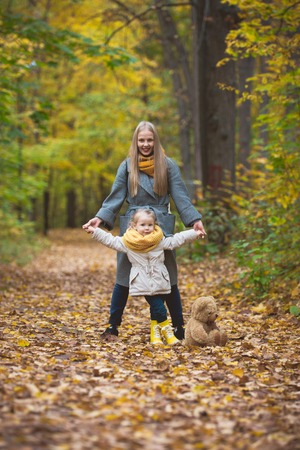 Mother and little daughter blonde walking and posing in autumn park, yellow lives around, telephotoの写真素材