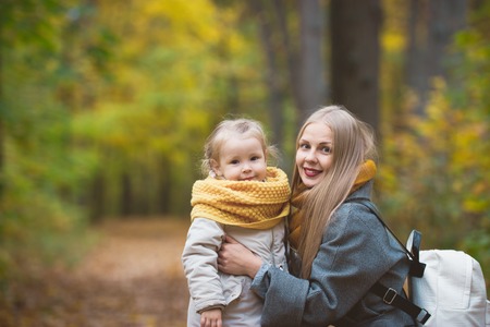 Happy family walking in autumn park - The mother and her daughter posing among the yellow leaves, telephotoの写真素材