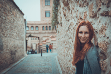 Outdoor portrait of attractive young woman with red hair standing at castle - tourist attraction, Segovia, Spainの写真素材