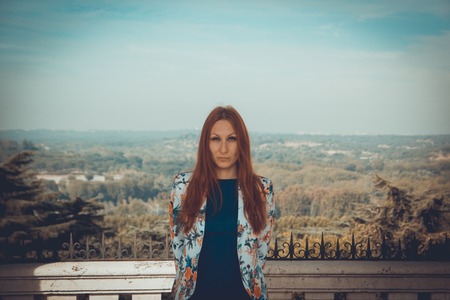 Outdoor portrait of attractive young woman with red hair standing - tourist attraction, great city...
