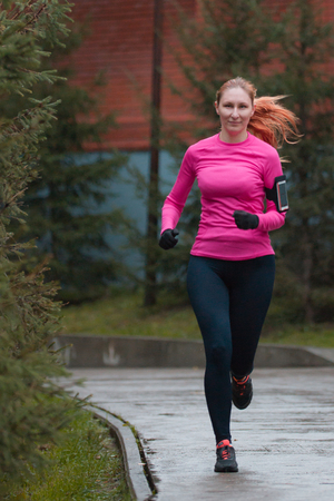 Woman in pink running in autumn park. Female runner outdoor, Healthy lifestyle. Caucasian fitness model.の写真素材