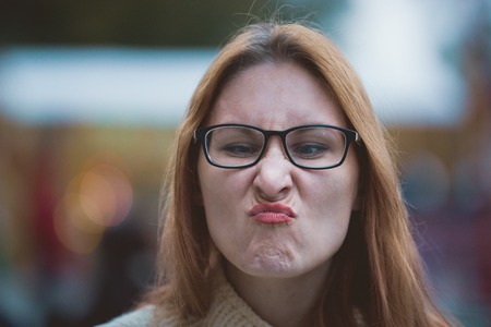 Young woman with glasses and red lips making faces, outdoor, close upの写真素材