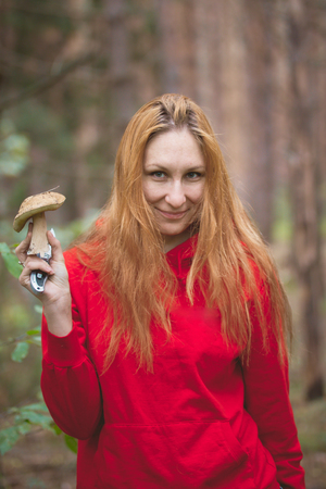 Young woman with red hair shows mushrooms boletus in the forest, telephotoの写真素材