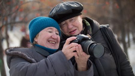 Two senior woman looking to they self photo camera and smiling at winter day, outdoor, outdoor, horizontalの写真素材