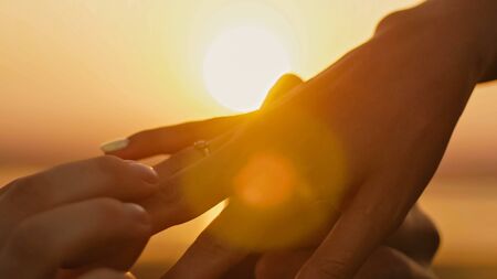 Wedding Ring Put On Finger Hands Touching Sunset Bride Groom Man Woman Marriage Proposal Vacation Honeymoon, close upの写真素材