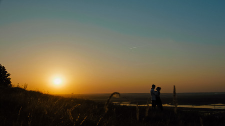 loving couple - brave young man and beautiful girl at sunset silhouette, over the sun, wide angle, slider shotの写真素材