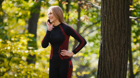 Young, sporty woman talking on cellphone and smiling at autumn park outdoor, close uptelephotoの写真素材