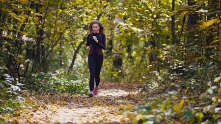 Young active female athlete exercising outdoor autumn park. Healthy women, telephotoの写真素材