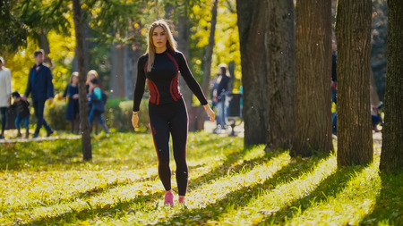 Sexy Attractive female blonde bikini-fitness model stretching in the autumn park on ground covered yellow leaves - stretching arms, telephotoの写真素材