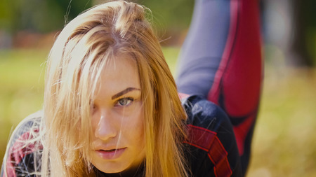 Sexy Attractive female blonde bikini-fitness model stretching in the autumn park - leg lifts, close up, telephotoの写真素材