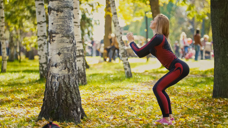 Sexy Attractive female blonde bikini-fitness model stretching in the autumn park on ground covered yellow leaves - sports squats, telephotoの写真素材
