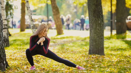 Sexy Attractive female blonde bikini-fitness model stretching in the autumn park on ground covered yellow leaves - legs flexibility, telephotoの写真素材