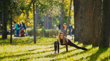 Fitness woman strength training doing workout at sunny autumn park. Fit caucasian sporty girl exercising her body, telephotoの写真素材