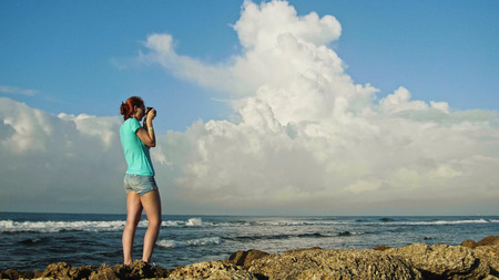 Young woman with red hair in glasses photographs sea standing on the rocks , beach of Dominican Republic, wide angle, Caribbean seaの写真素材