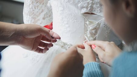 bridesmaid buttoning dress at bride's home, close upの写真素材