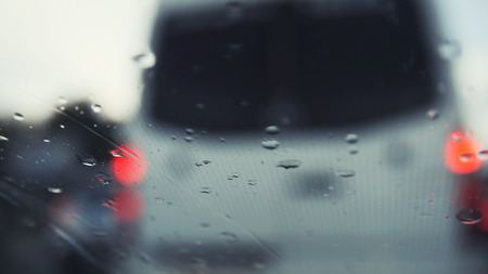 Car glass on a rainy day - defocused background. Moving waterdrops in the wipers of the windshield,...