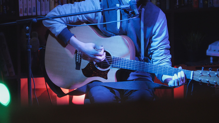 Guitarist plays acoustic guitar and sings microphone in night club, blue lights, close up, telephoto