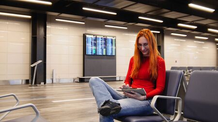 Young attractive woman with red hair and glasses use gadget in airport departure loungeの写真素材