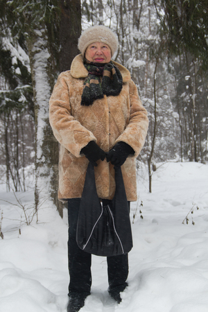 Portrait of senior woman fur coat and hat standing in cold winter snow covered forest, close upの写真素材