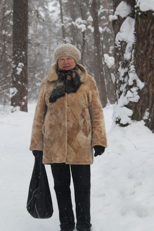 Portrait of old lady fur coat and hat standing in cold winter snow covered forestの写真素材