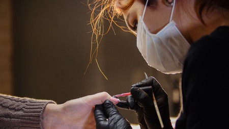 Manicure in beauty salon - cosmetic master in medical mask deals polish on the nailsの写真素材