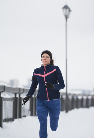 Fitness girl model running at snow winter promenade, joggingの写真素材