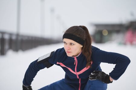 Woman runner stretching legs before run at snow winter promenade, close upの写真素材
