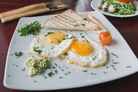 Fried eggs on white plate with green and tomato cherry - breakfastの写真素材