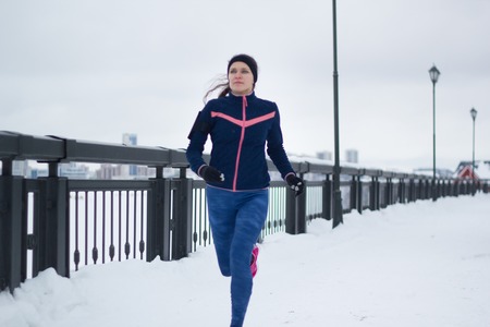 Young caucasian woman fitness model running at snow winter promenadeの写真素材
